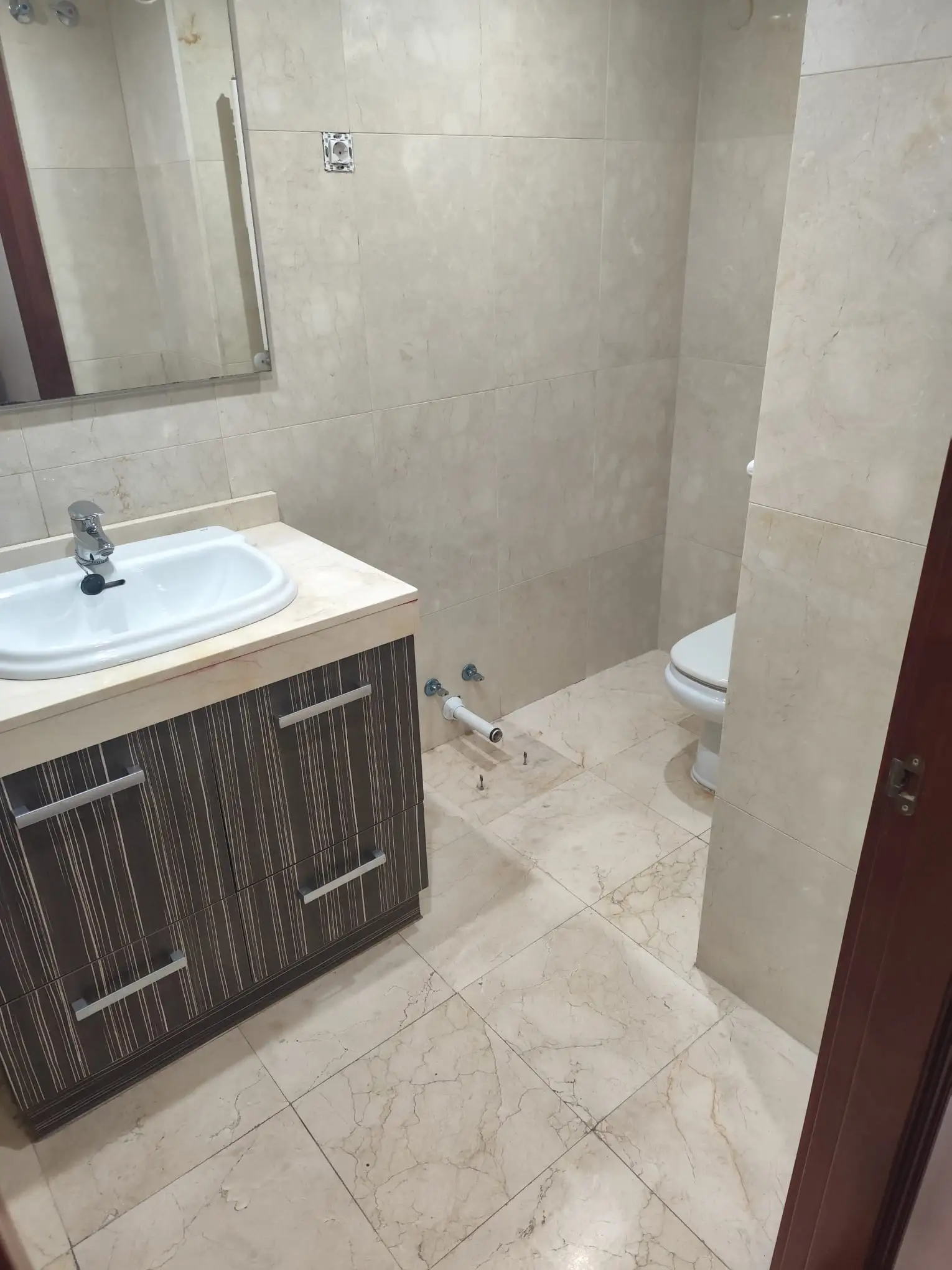 Reforma de baño con mueble de madera oscura, lavabo blanco y revestimiento cerámico beige en Etxebarri